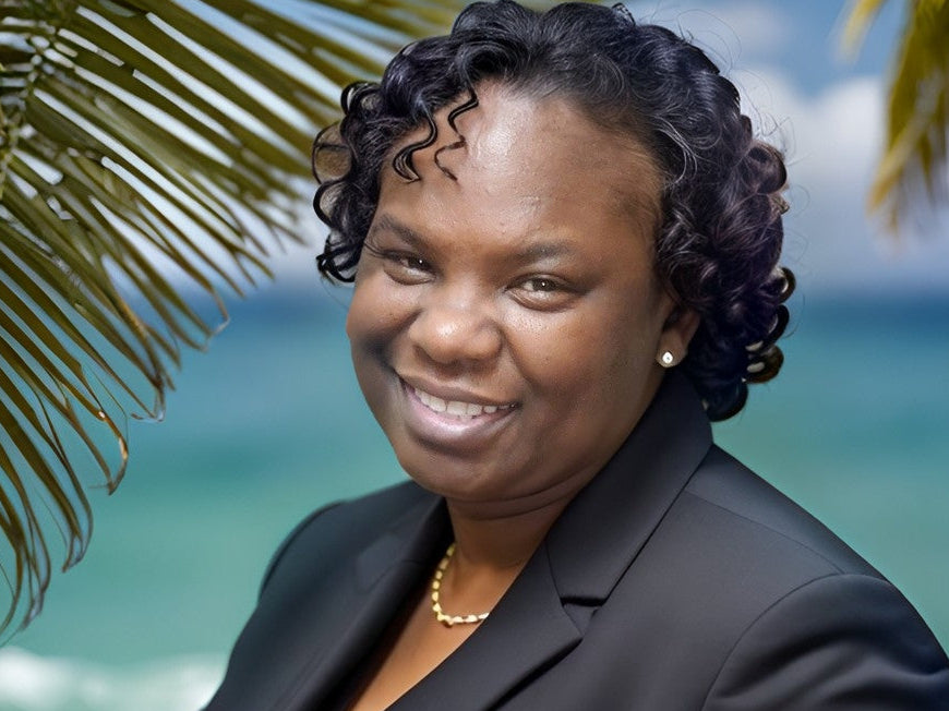 Woman in a black blazer standing in front of palm leaves with a blurred beach background